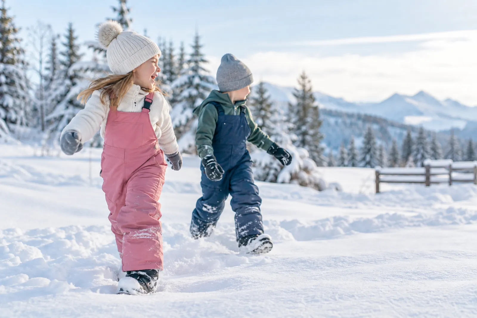 Two kids in colourful snow bibs and snow pants standing in fresh snow on a bright winter morning